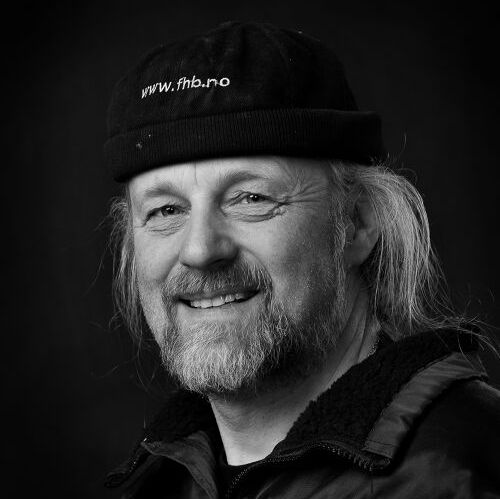 Mann med svart lue og jakke smiler.